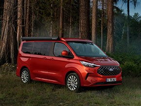 Ein roter Familienvan steht im Wald, umgeben von hohen Bäumen und natürlicher Landschaft.